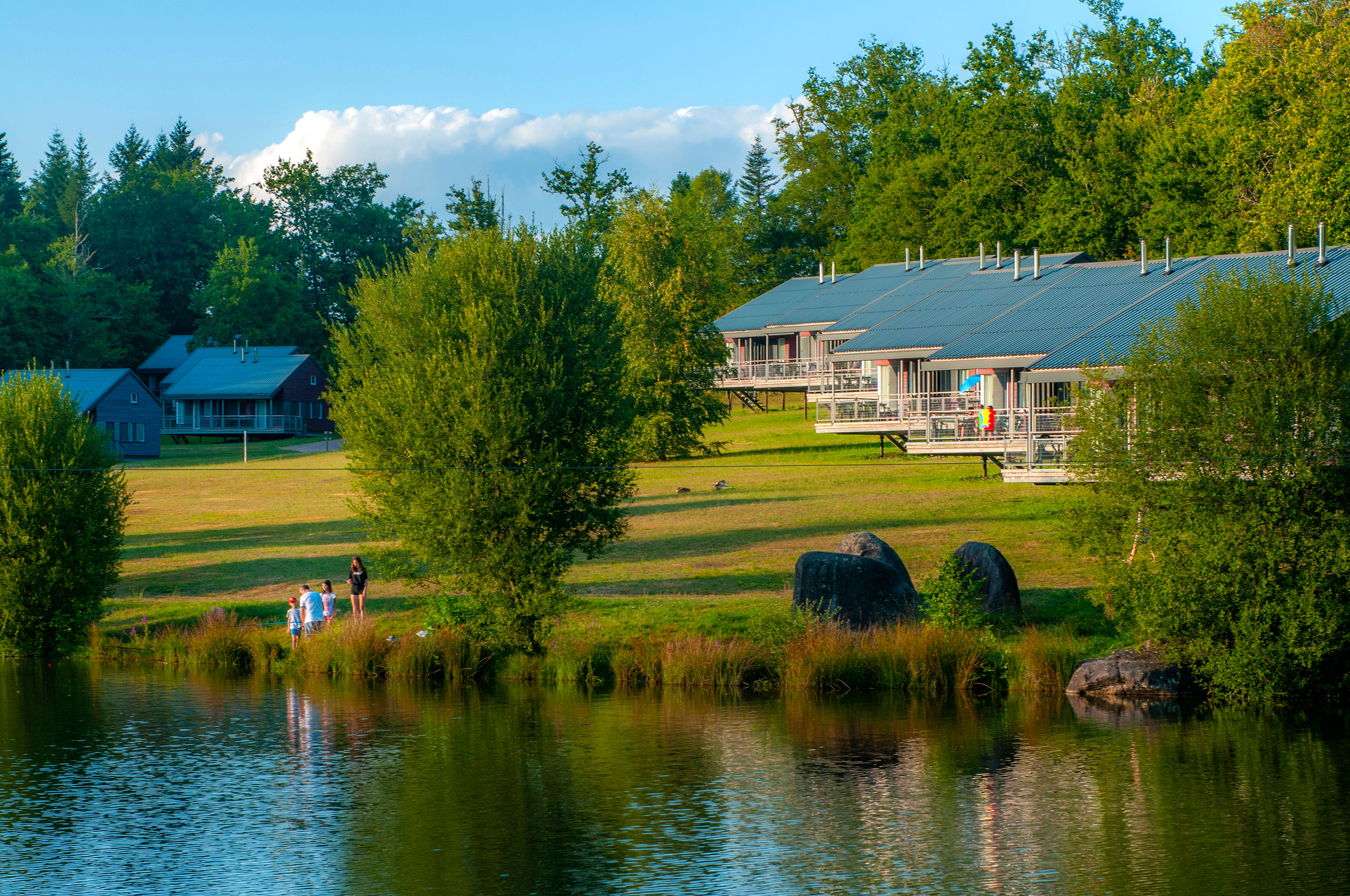 image Families by the water's edge, with the stilt chalets and blue sky behind them.