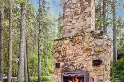 Stone outdoor fireplace with a built-in bench, surrounded by trees and natural stonework