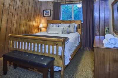 Sunlit bedroom with wooden accents, a bench at the foot of the bed, and forest views outside
