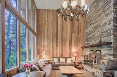 Floor-to-ceiling windows frame forest views from the living area with stone fireplace and plush sofas