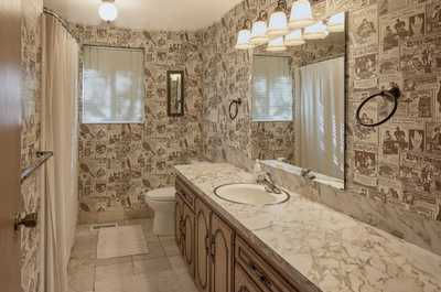 Classic patterned wallpaper surrounds dual marble sinks, with six light fixtures above the mirror