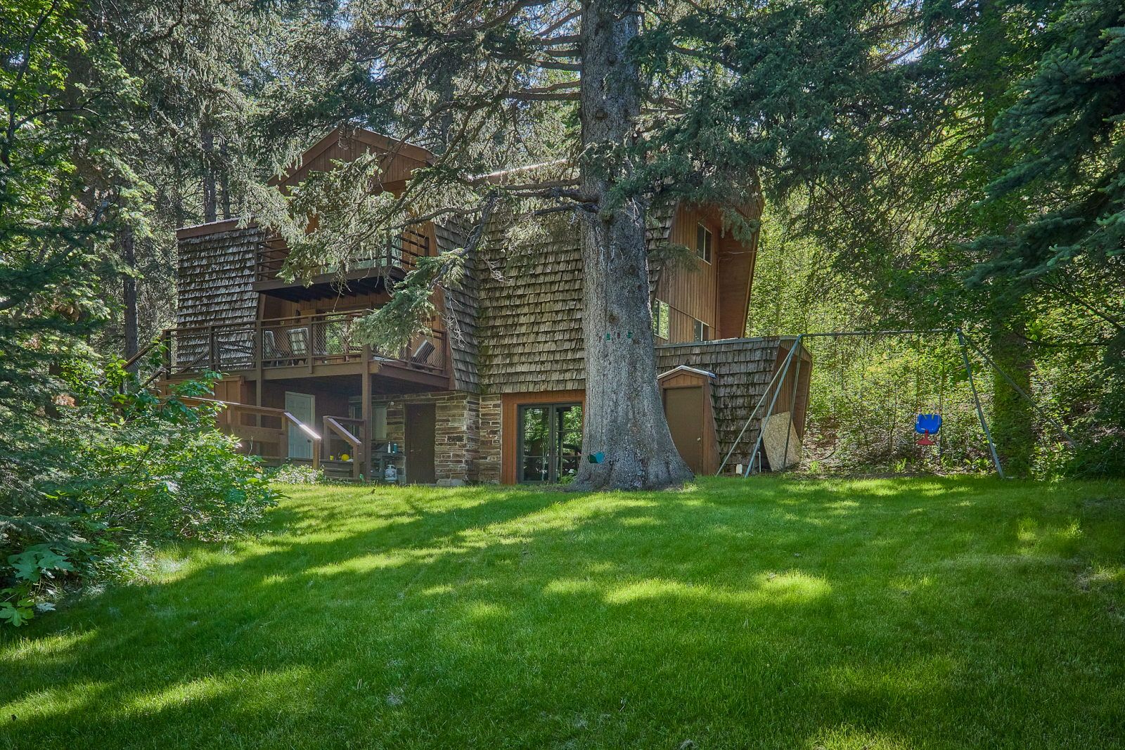 image Timber-clad cabin set in a grassy clearing, with forested hillside and outdoor deck visible