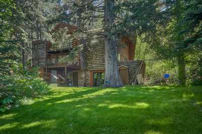 Timber-clad cabin set in a grassy clearing, with forested hillside and outdoor deck visible