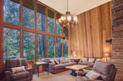 High-ceilinged living room with dramatic floor-to-ceiling windows, wooden walls, and two sofas