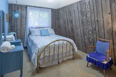 Blue bedroom with floral bedding, gold metal bed frame, and a small chair beside the window