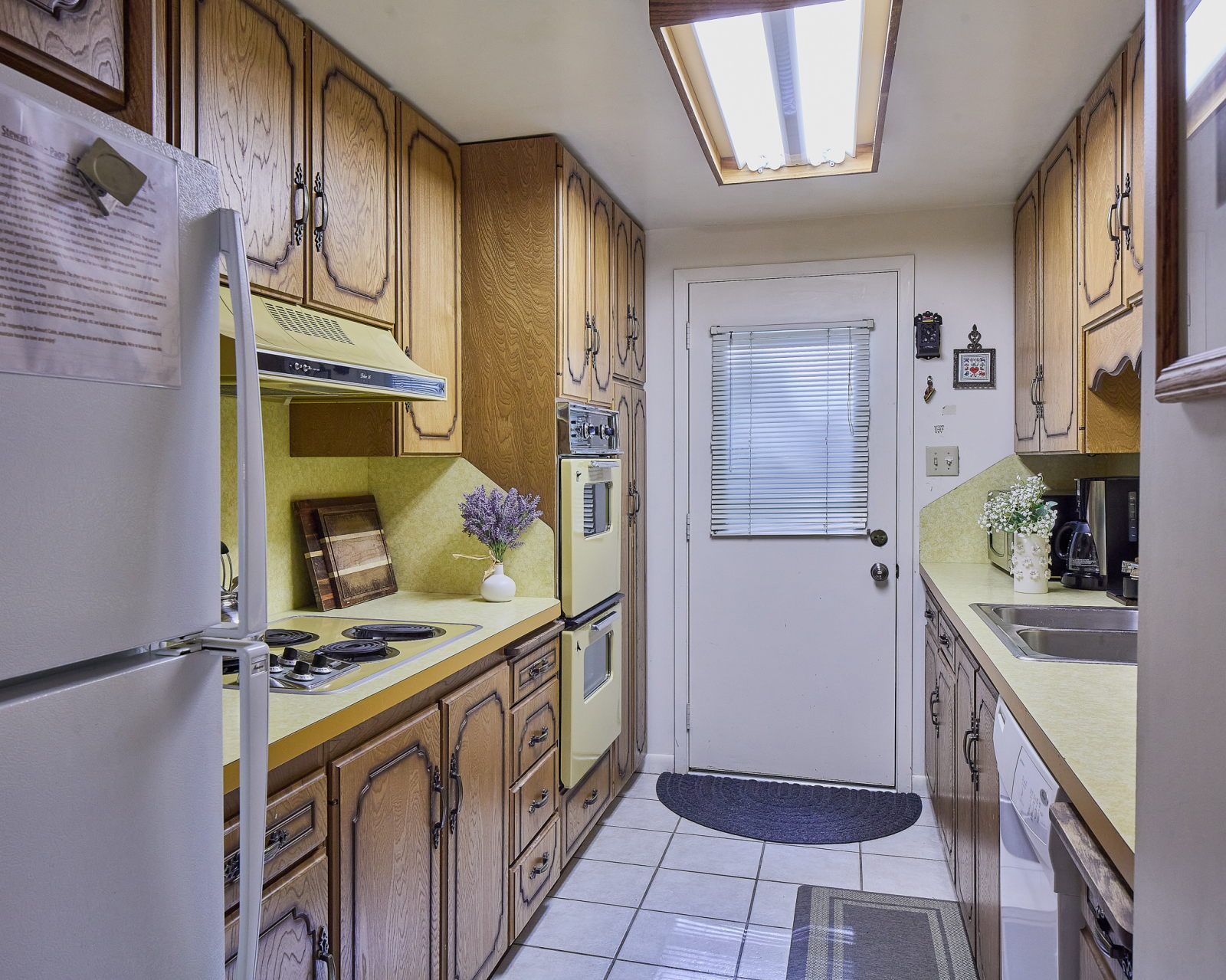 image Oak cabinets, yellow countertop, and tile floor make up the main kitchen with door leading outside