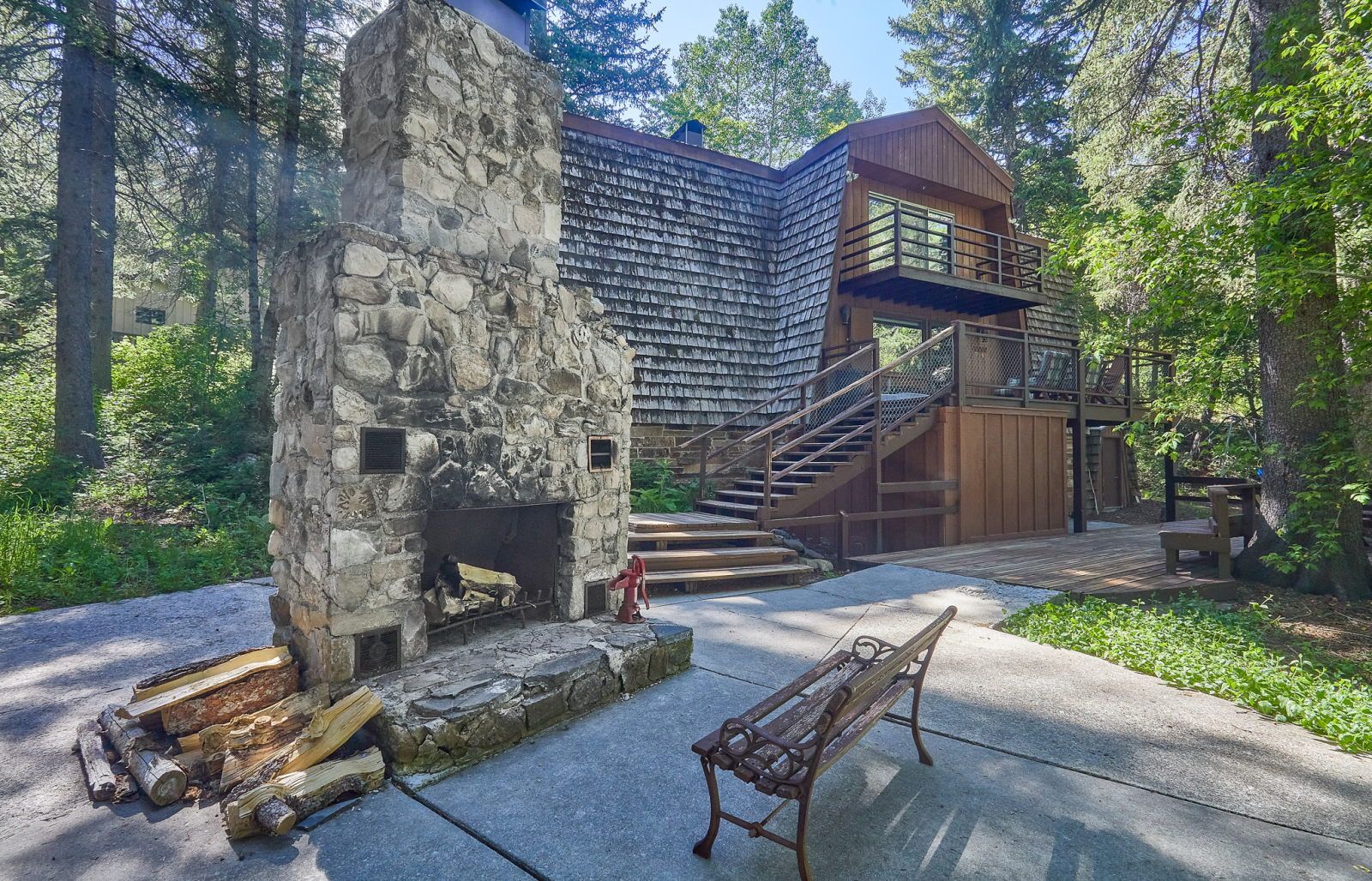 image Stone outdoor fireplace and metal bench sit beside the cabin steps, backed by dense forest