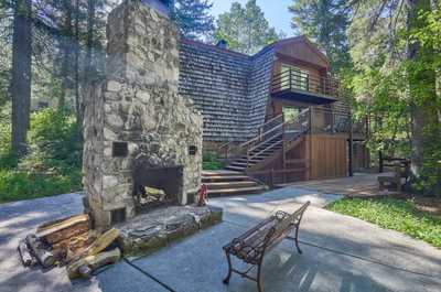 Stone outdoor fireplace and metal bench sit beside the cabin steps, backed by dense forest