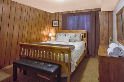 Wood-paneled bedroom with a double bed, plush carpet, bedside lamp, and warm-toned linens