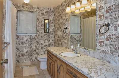 Second view of the marble-top vanity with patterned wallpaper and multiple overhead light fixtures
