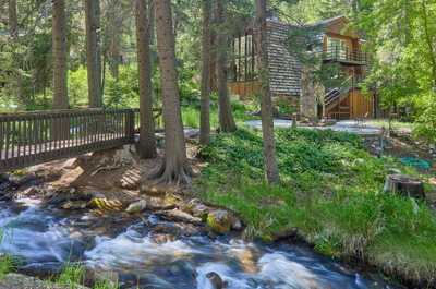 Outdoor stone fireplace with log bench sits among tall trees beside the cabin