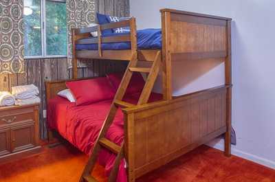 Wooden bunk bed with blue and red bedding, patterned curtains, and warm overhead lighting