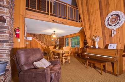 Leather armchair sits beside the stone fireplace, with stairs rising to the loft behind