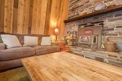 Plush sofa with light cushions faces the stone fireplace, with a warm lamp and wooden side table