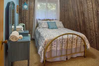 Blue walls and patterned bedspread on a gold frame, with a vintage dresser and wood paneling