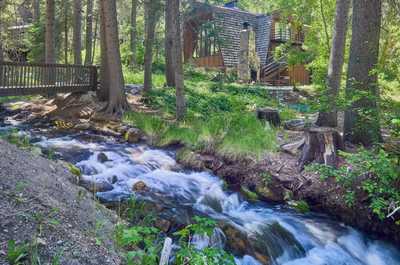 Stone chimney and cabin exterior framed by forest, with the stream cascading nearby