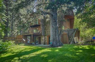 Five-bedroom cabin with wooden shingles nestled in trees, expansive lawn and private outdoor deck
