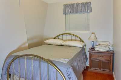 Gold metal twin bed with gray linens on orange carpet, under soft overhead lighting