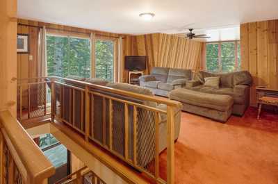 Upper lounge with multiple sofas, pine-paneled walls, ceiling fan, and windows on three sides