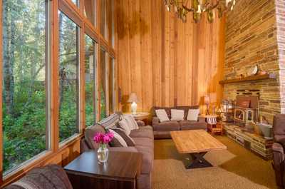 Large windows reveal a lush forest view, with comfortable seating and a wooden coffee table