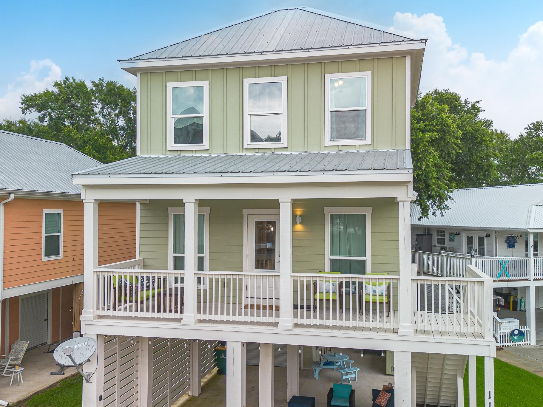 image Elevated beach house with green board-and-batten siding, white wraparound porch railing, and a covered lower entertainment area