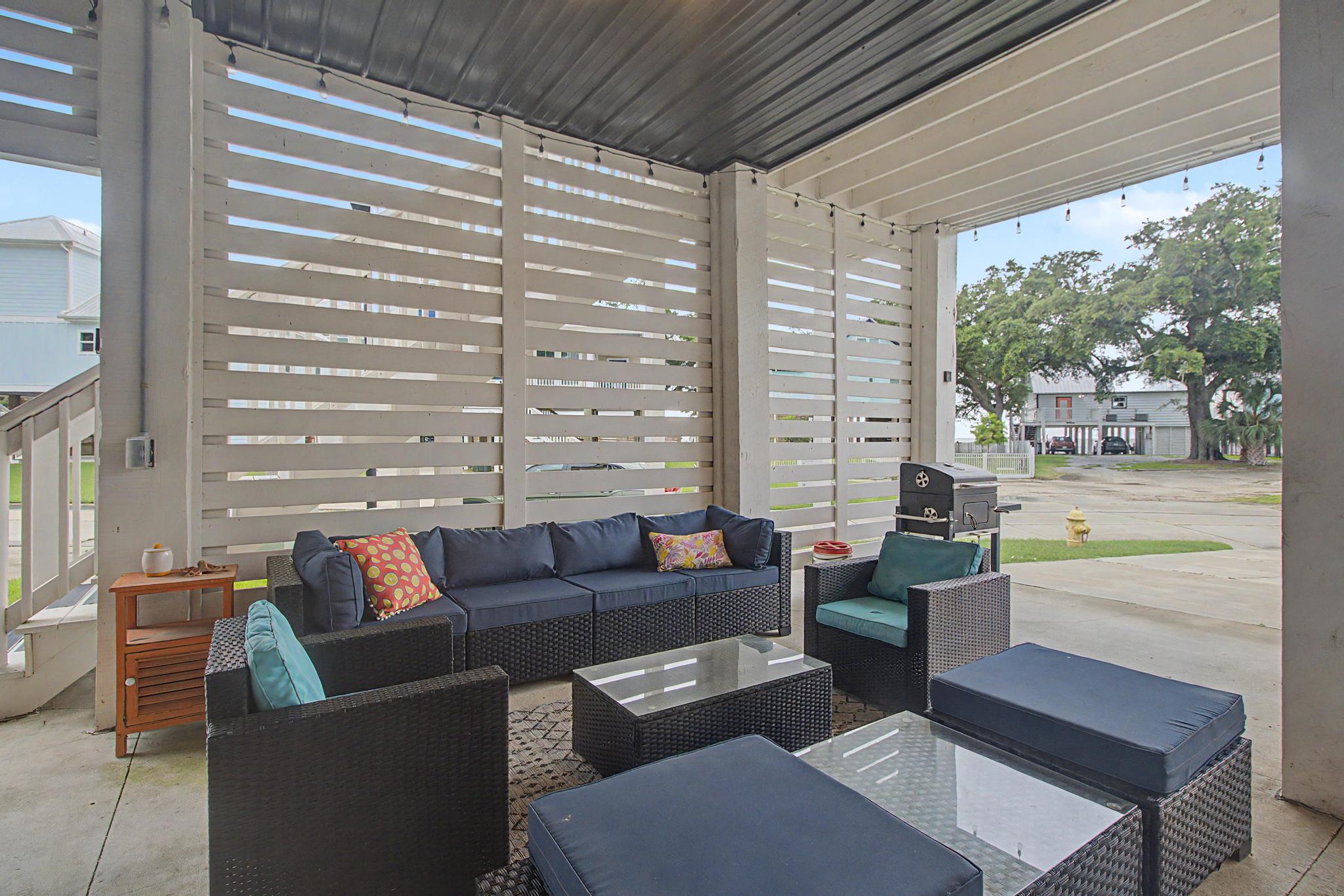 image Covered lower-level patio with sectional seating, a charcoal BBQ grill, and a slatted privacy wall on concrete