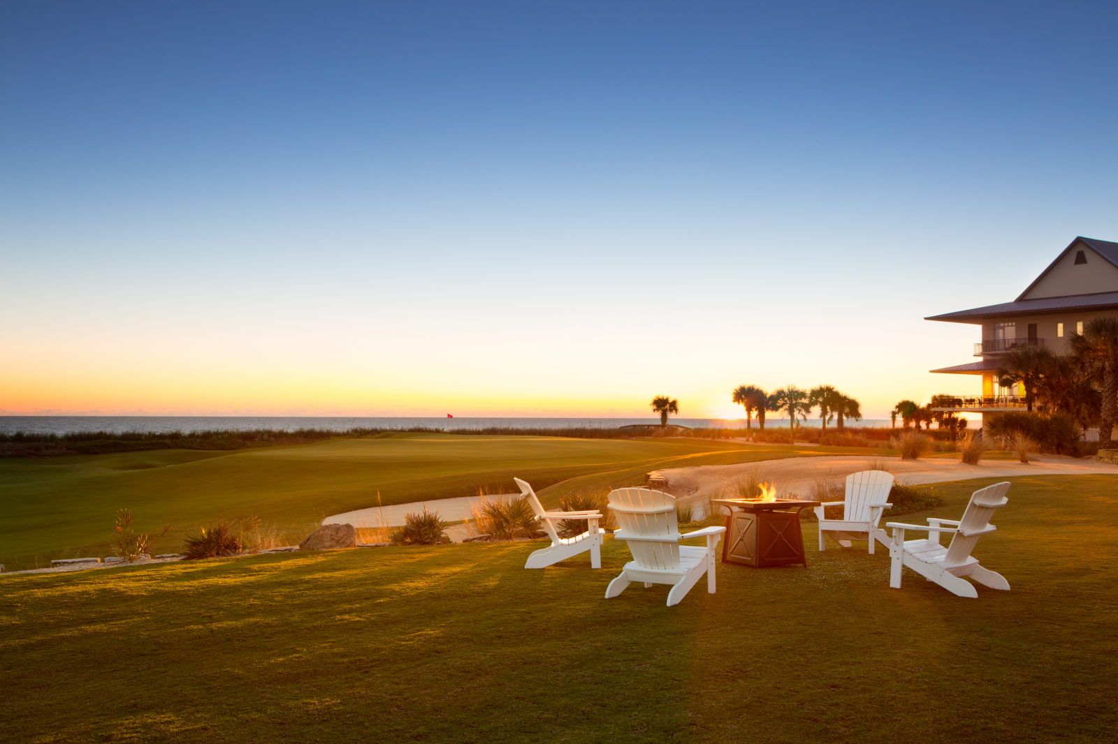 image White lounge chairs arranged around a fire pit on the golf course at sunset