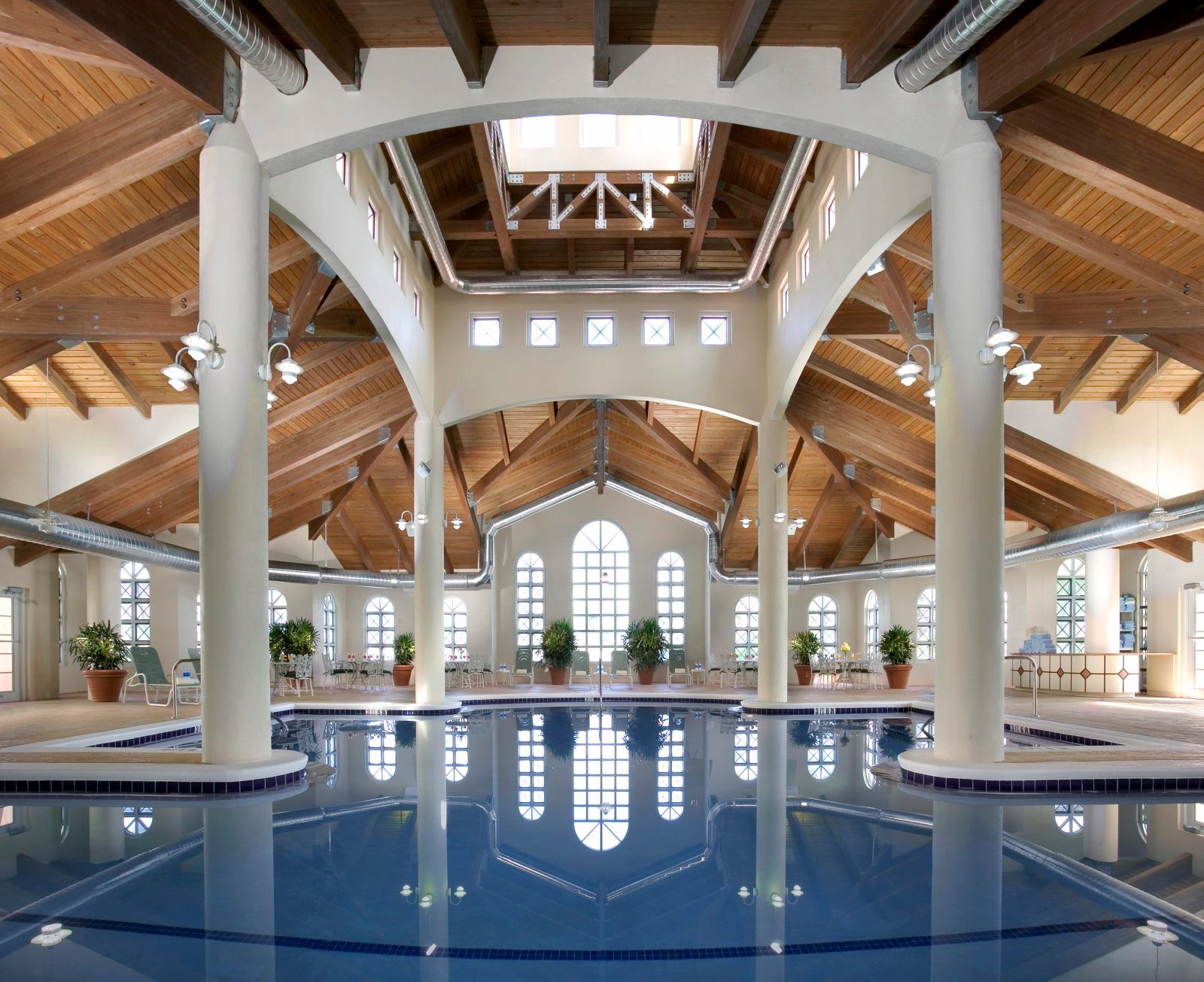 image Indoor pool reflecting the wooden-beam ceiling, white columns, potted plants, and hanging light fixtures