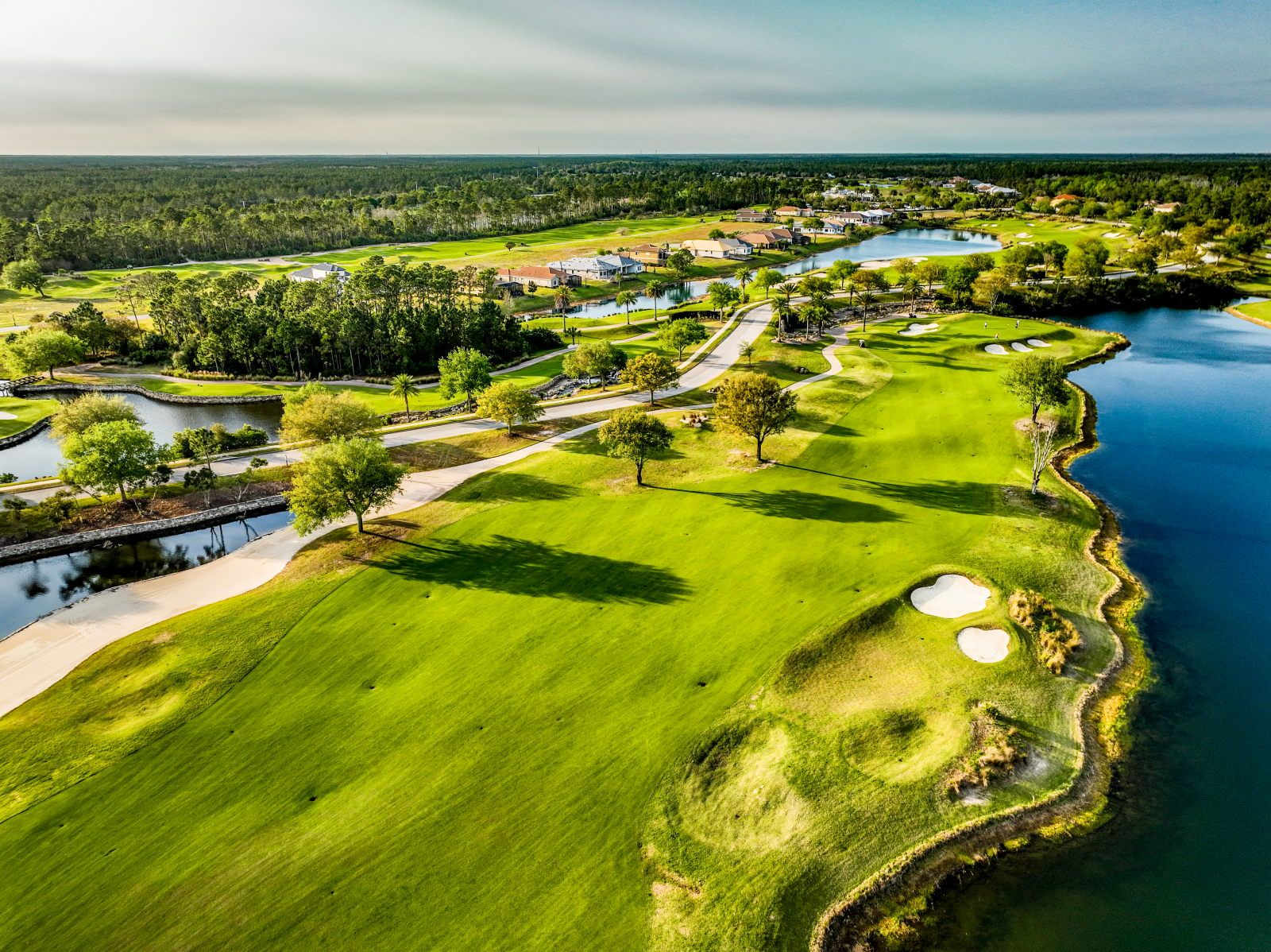 image Aerial view of a golf course fairway with a water hazard, sand bunkers, and tree-lined residential buildings beyond