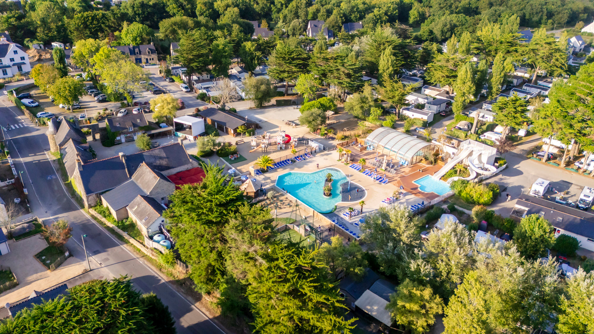 image Aerial view of the outdoor pool area, water slide, sun loungers and surrounding greenery.