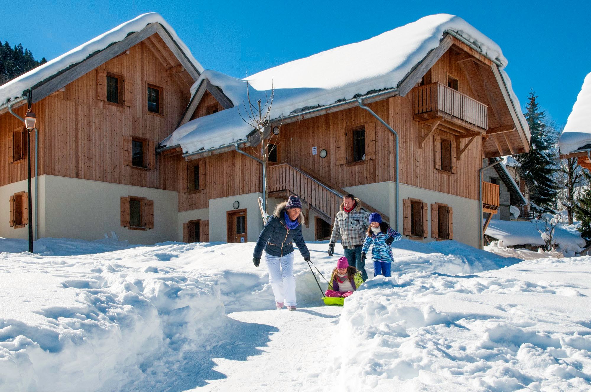 image Family walking in the snow with sledding equipment near chalets