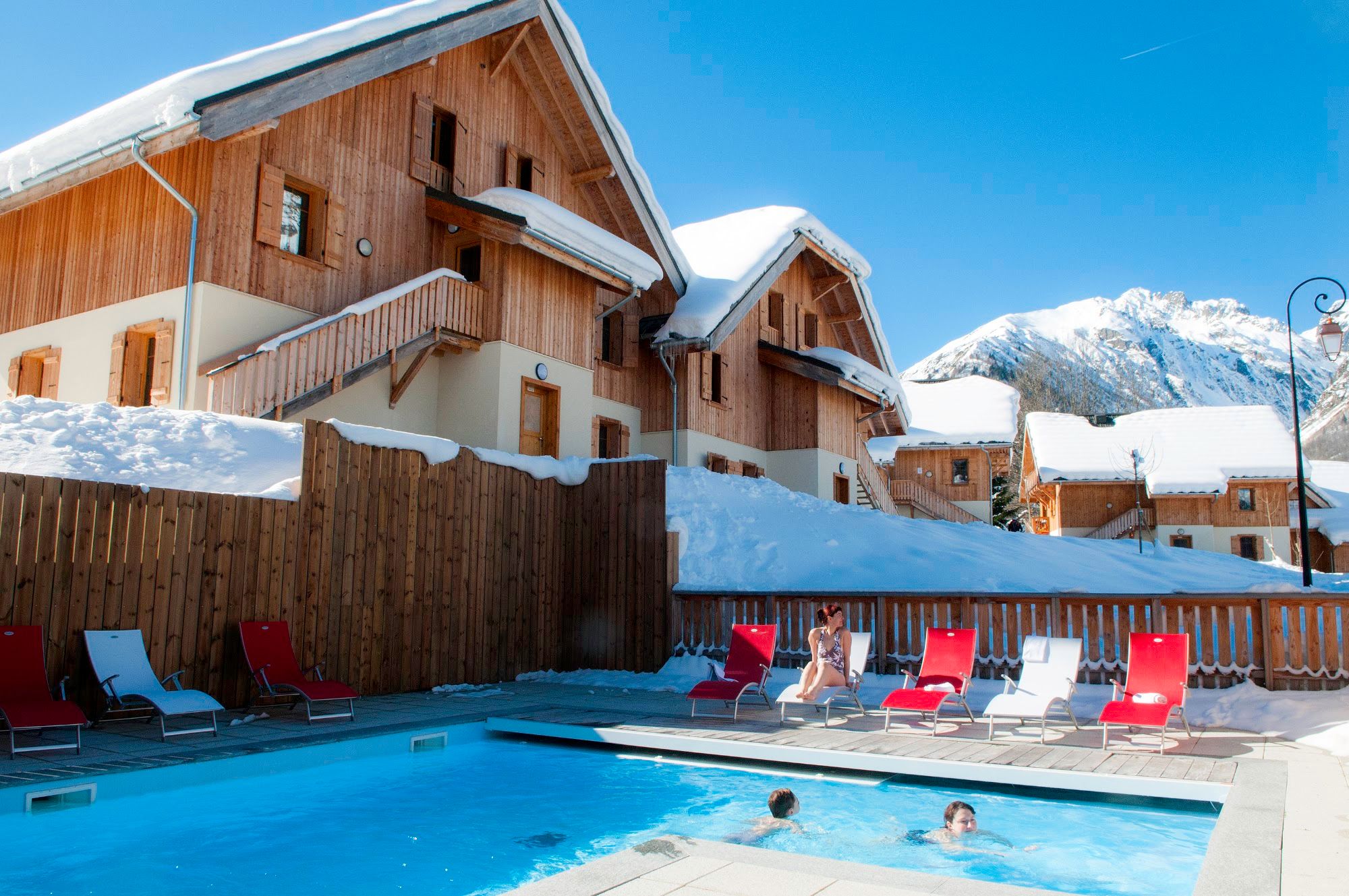 image Outdoor pool with lounge chairs beside chalets and mountains