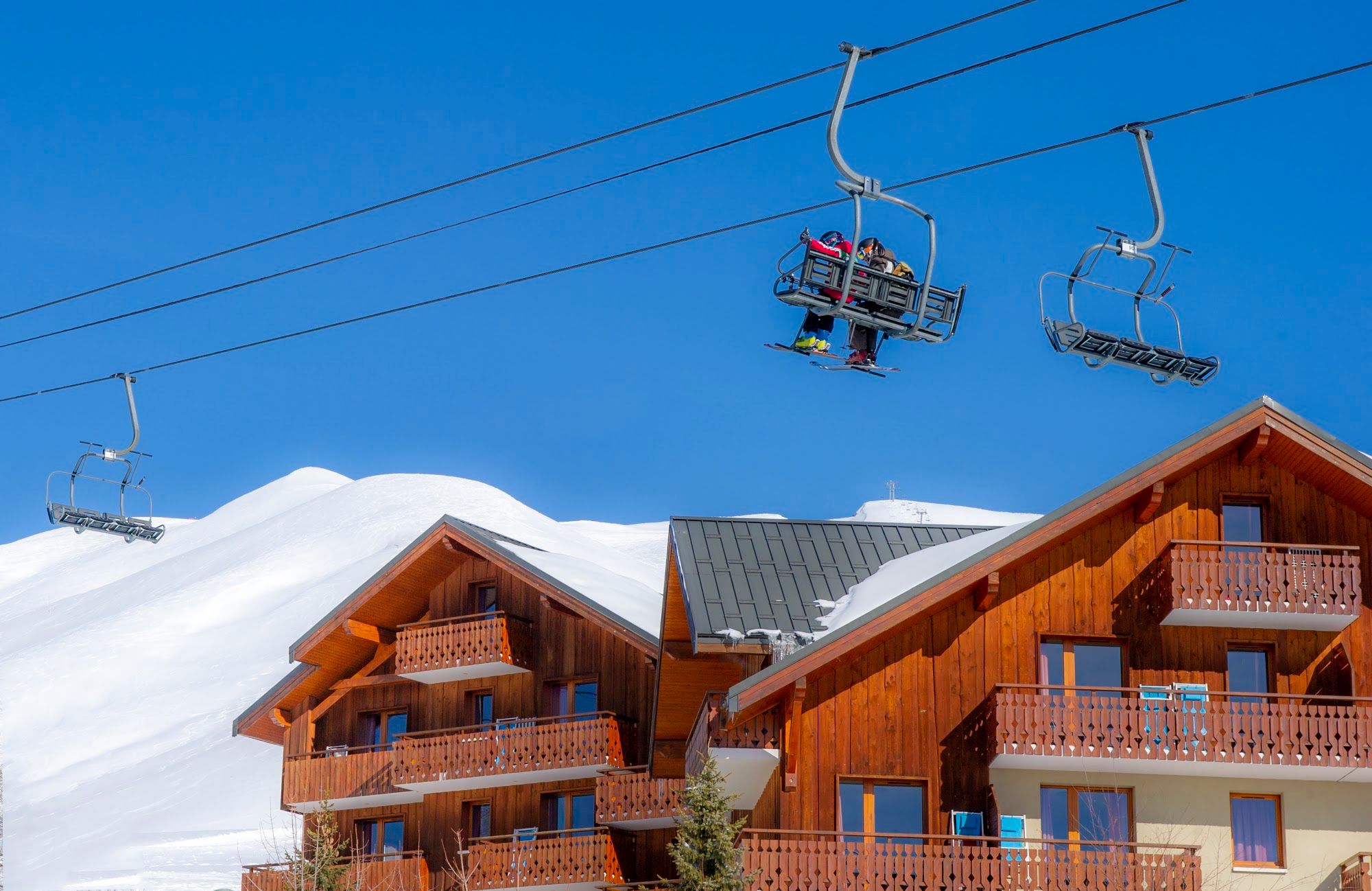 image Skiers on a lift with wooden chalets and snowy mountains.