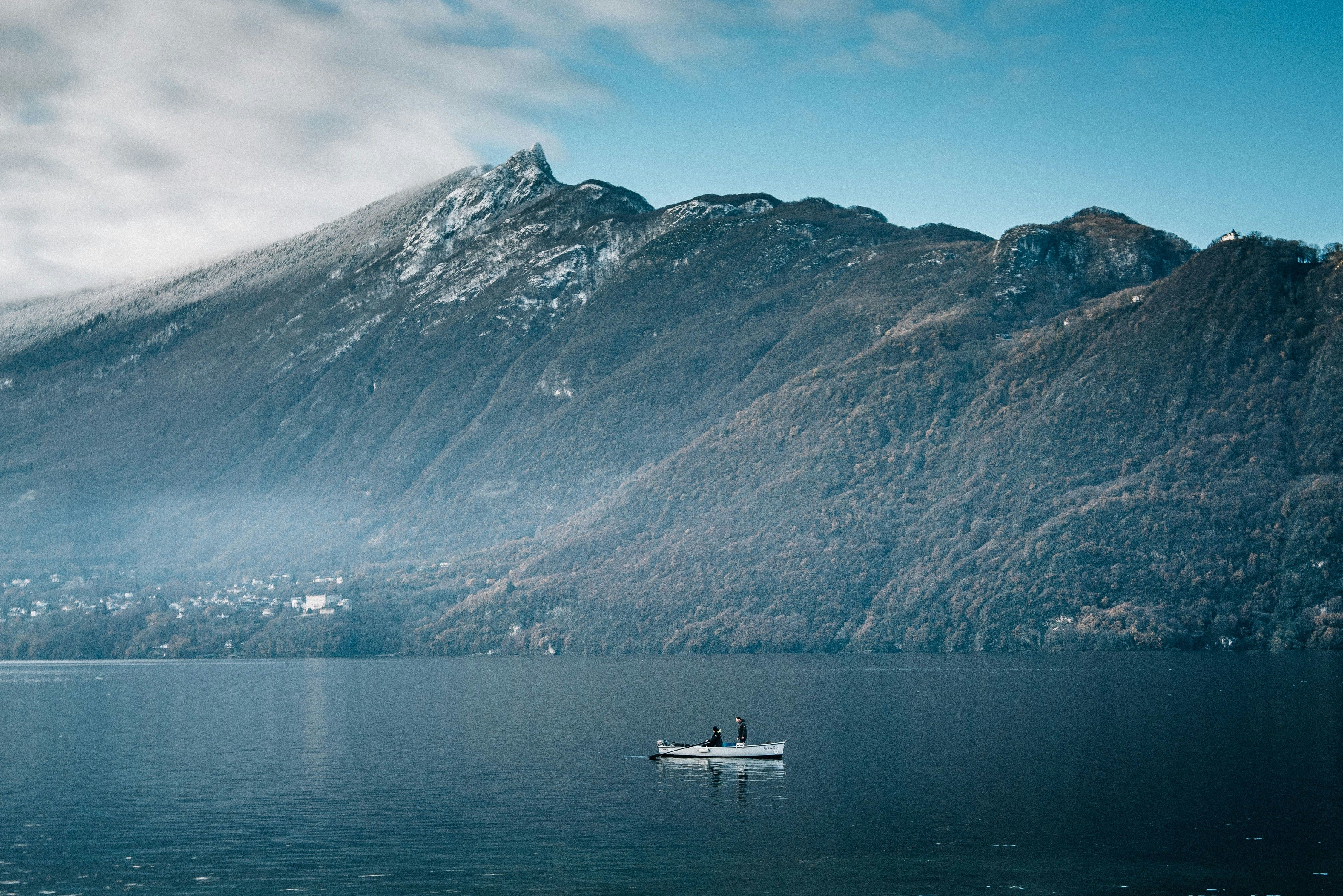 image Two fishermen in a boat on a tranquil lake with mountains nearby.