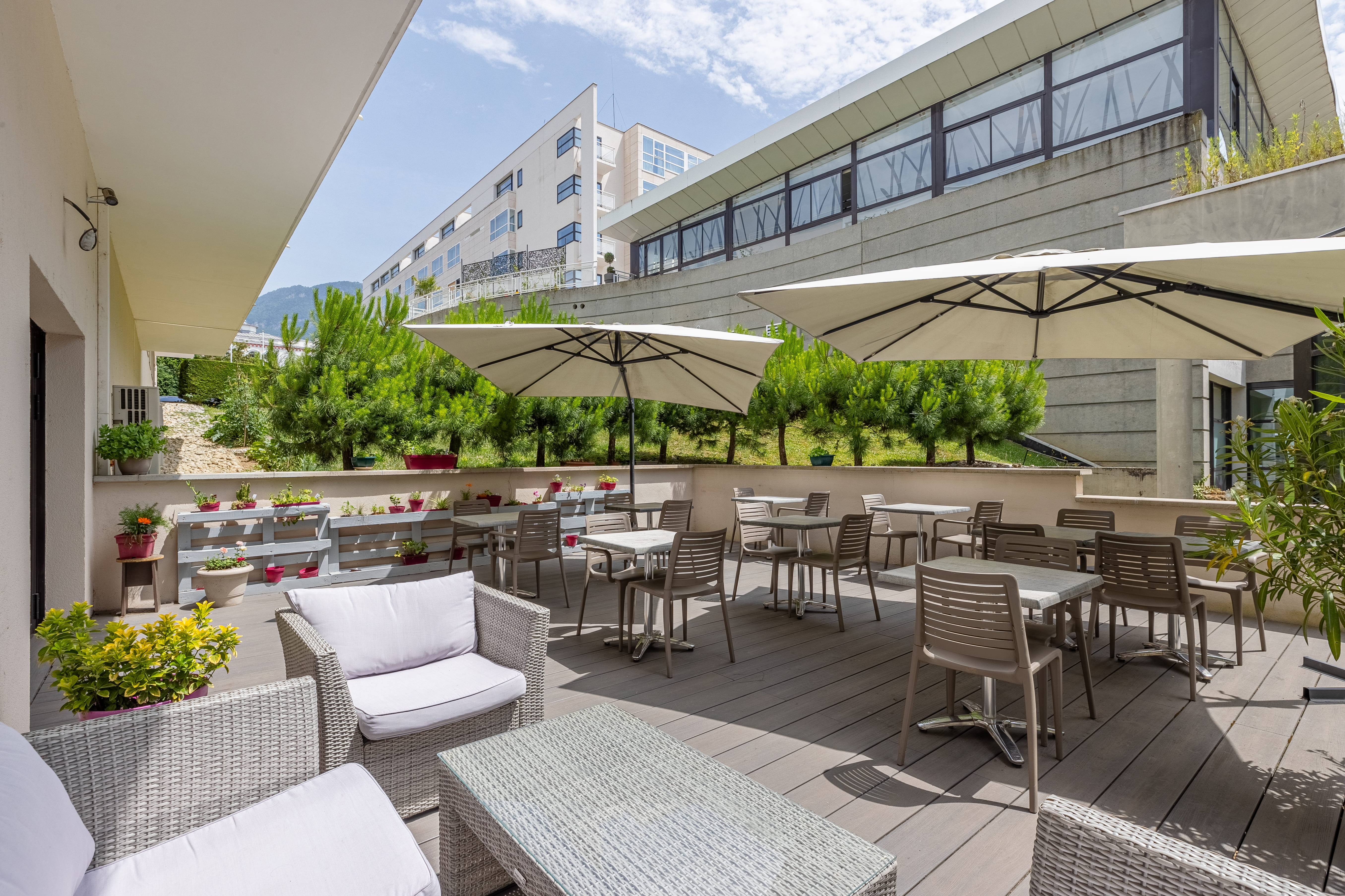 image Outdoor seating area with tables under umbrellas, surrounded by greenery.