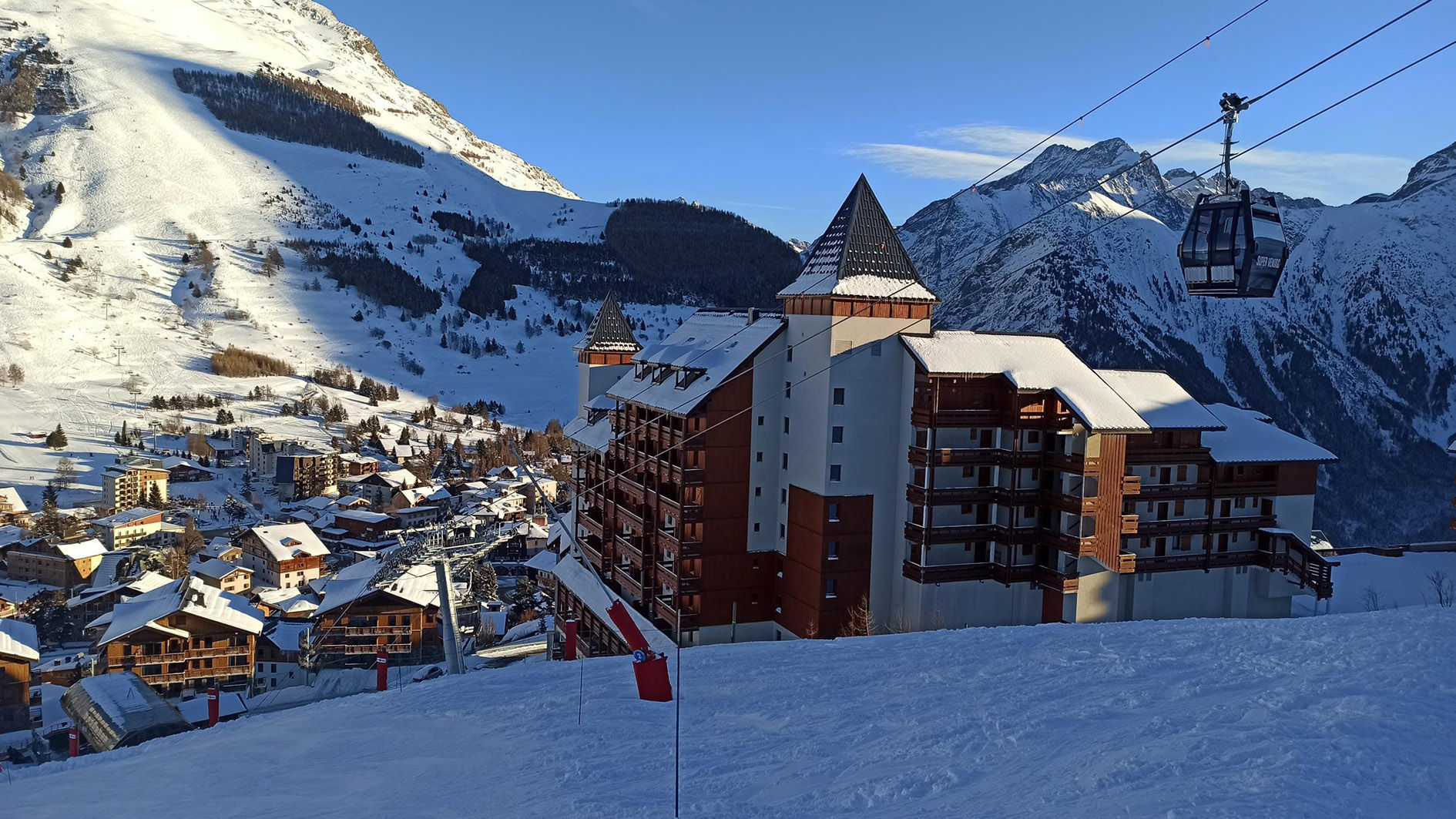 image Snow-covered chalets and a gondola rising toward the pistes.