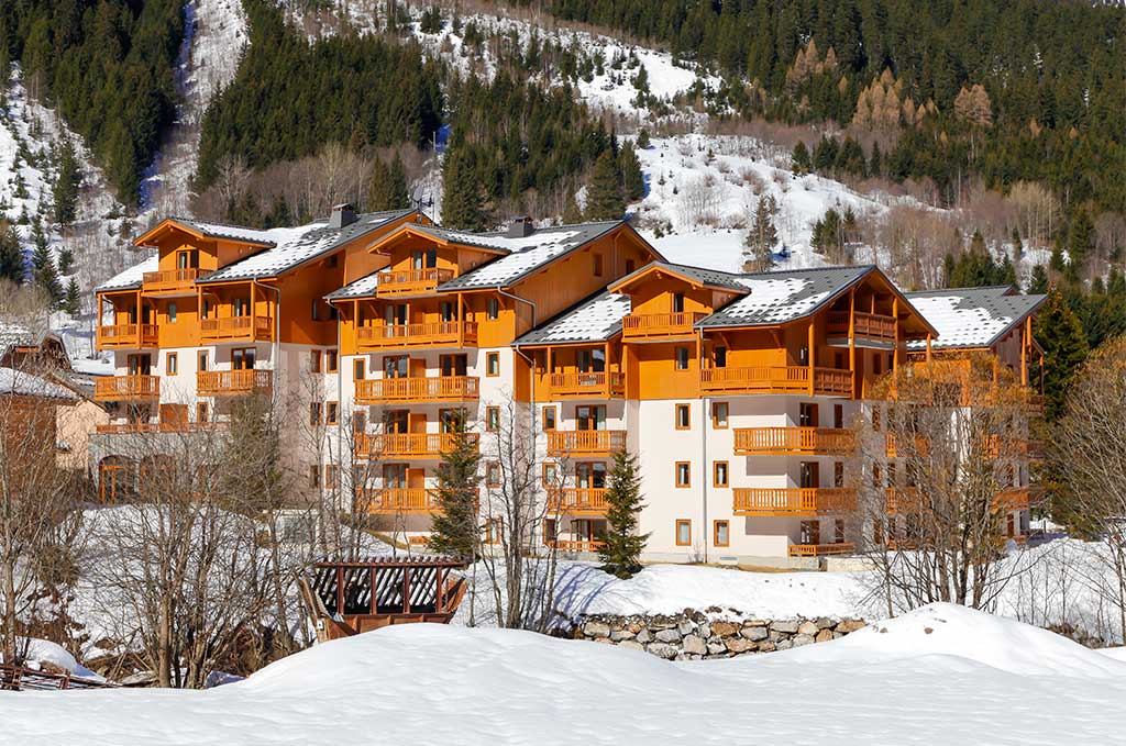 image A closer winter view of the chalet-style facades, backed by snow-dusted pine forest.
