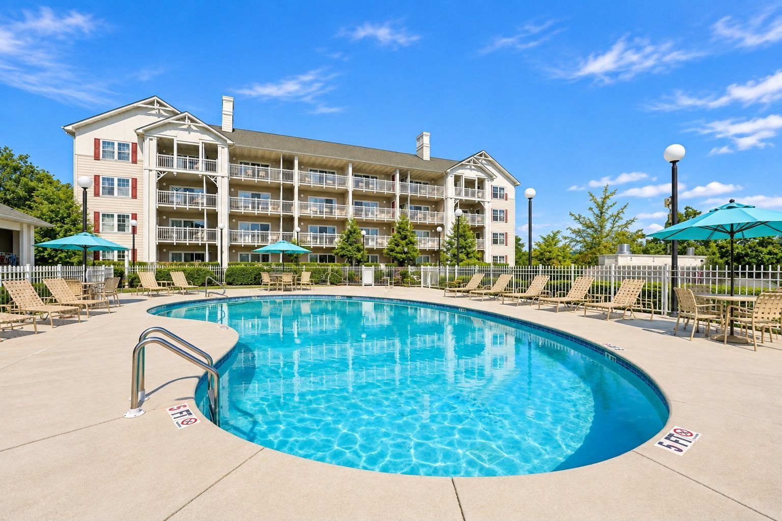image Outdoor pool with lounge chairs, umbrellas, and a multi-story building with balconies in the background