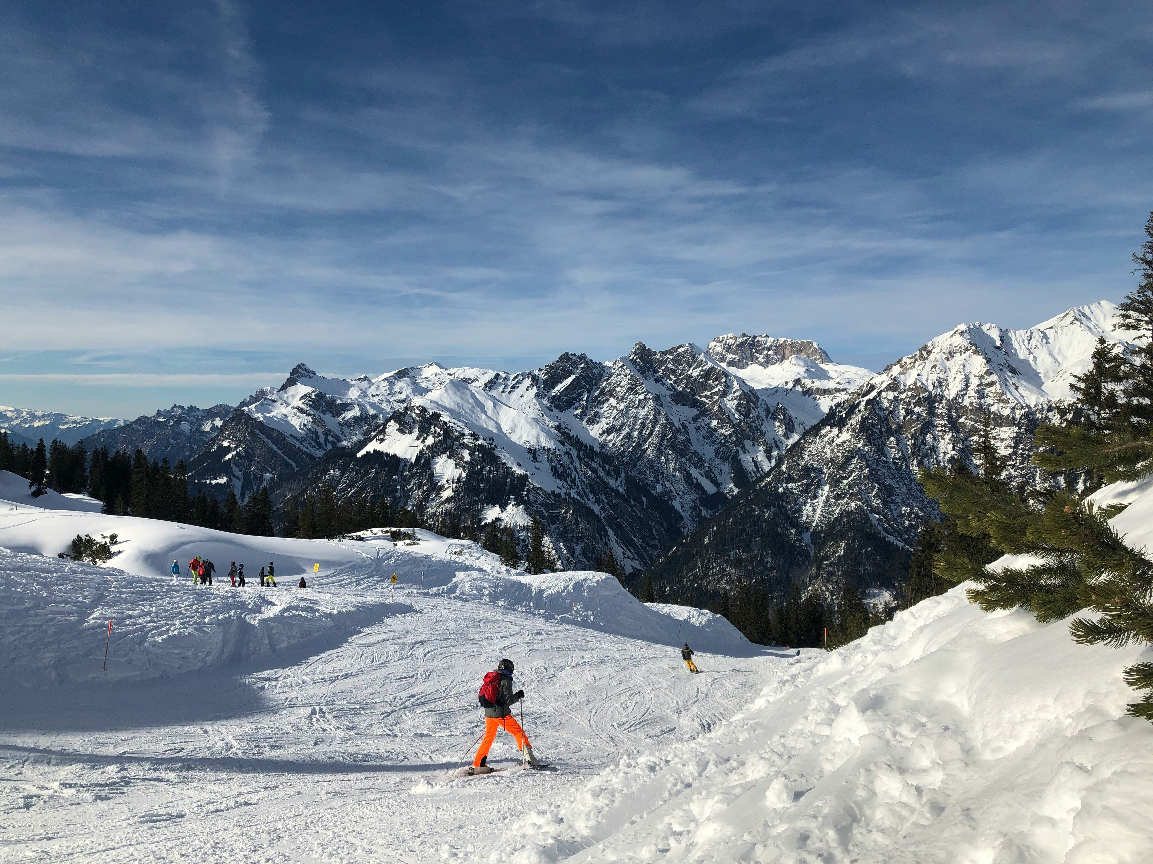 image Skiers carve down snowy pistes beneath big mountain views.